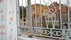 A view through a metal gate with a patterned curtain, a balcony, and a building with a red roof and beige walls. - B&B Casa AriGiLi (Fuengirola)