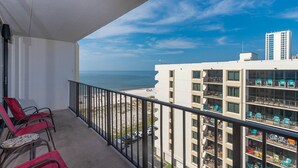 Ein Balkon mit roten Stühlen, Blick auf den Strand und ein Gebäude mit Balkonen.