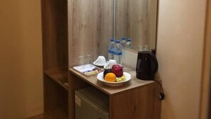 A compact kitchenette with a wooden cabinet, a small refrigerator, a coffee maker, and a plate of fruit.