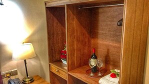 A wooden wardrobe with two open shelves, a bedside table with a lamp, a telephone, and a wine bottle.
