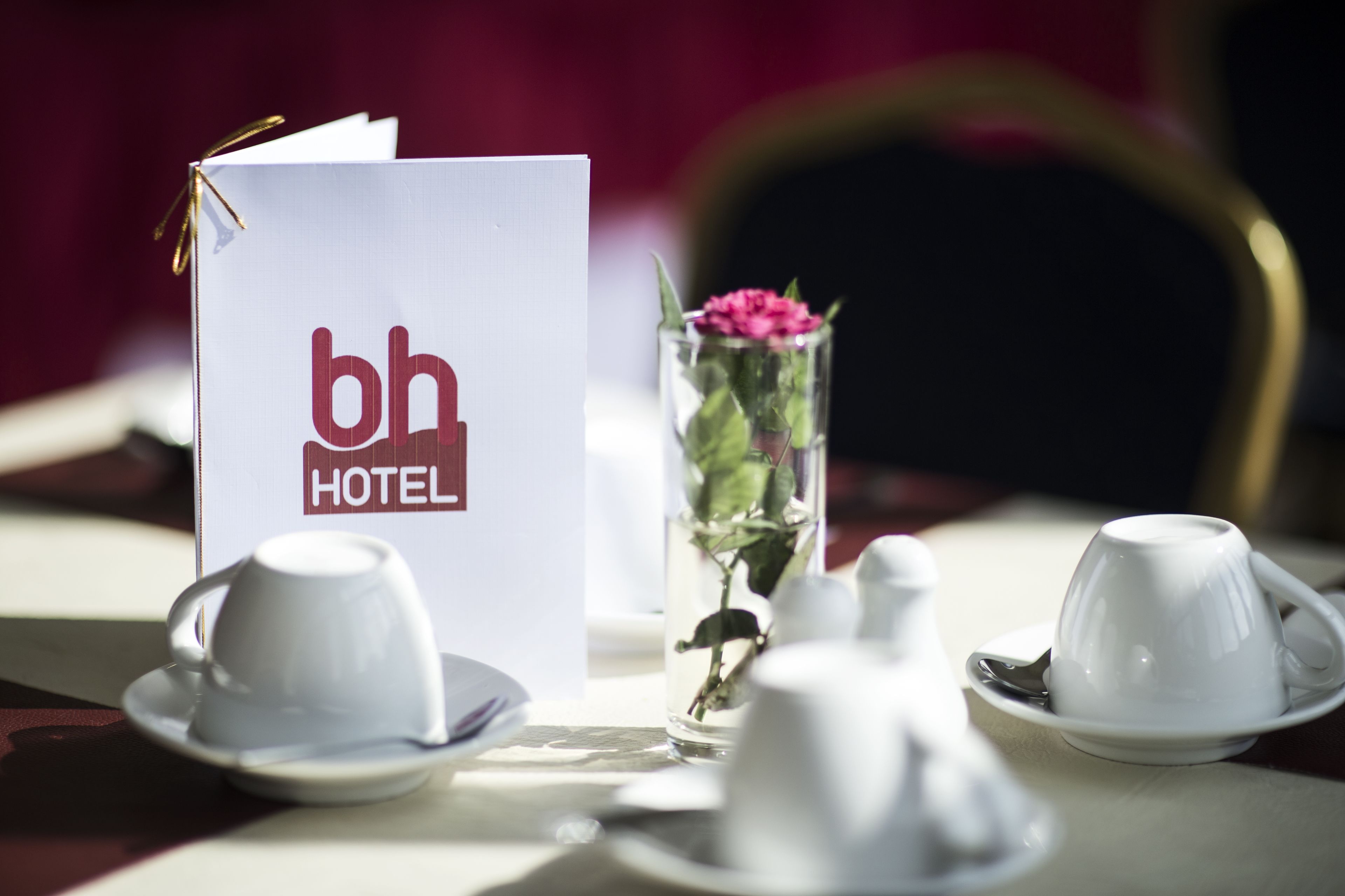 A hotel room with a table set for tea, a glass of flowers, and a 'bh HOTEL' sign.