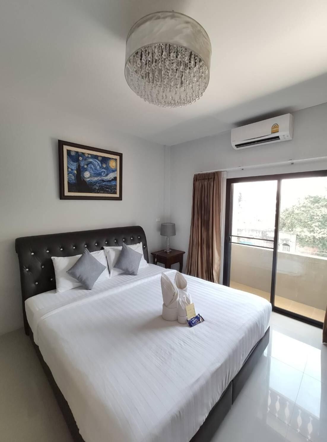Une chambre d’hôtel avec un grand lit, un lustre, un appareil de climatisation, un tableau et une vue sur l’extérieur.