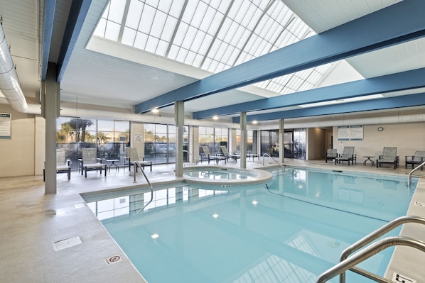 An indoor swimming pool with clear glass ceilings, lounge chairs, and a view of the outdoors.