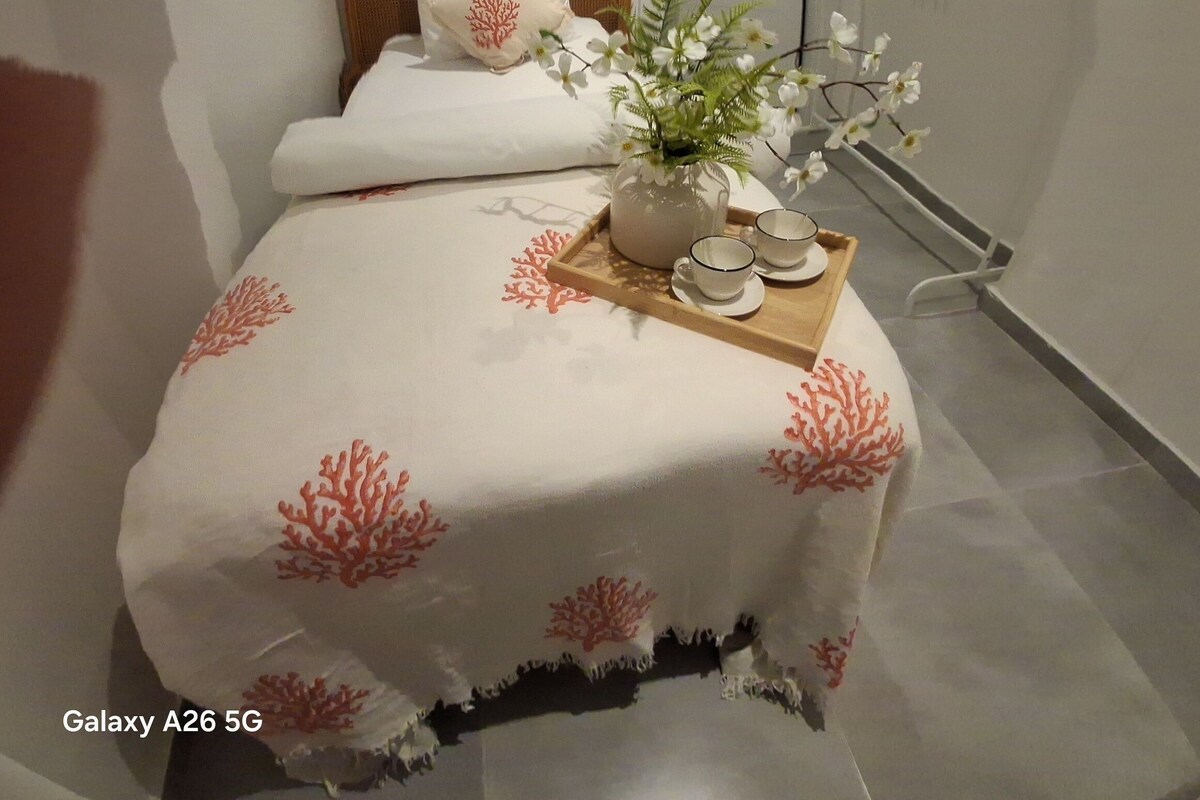 Ein Schlafzimmer mit einem Bett, einem Nachttisch mit Blumenvase und einer Tür.