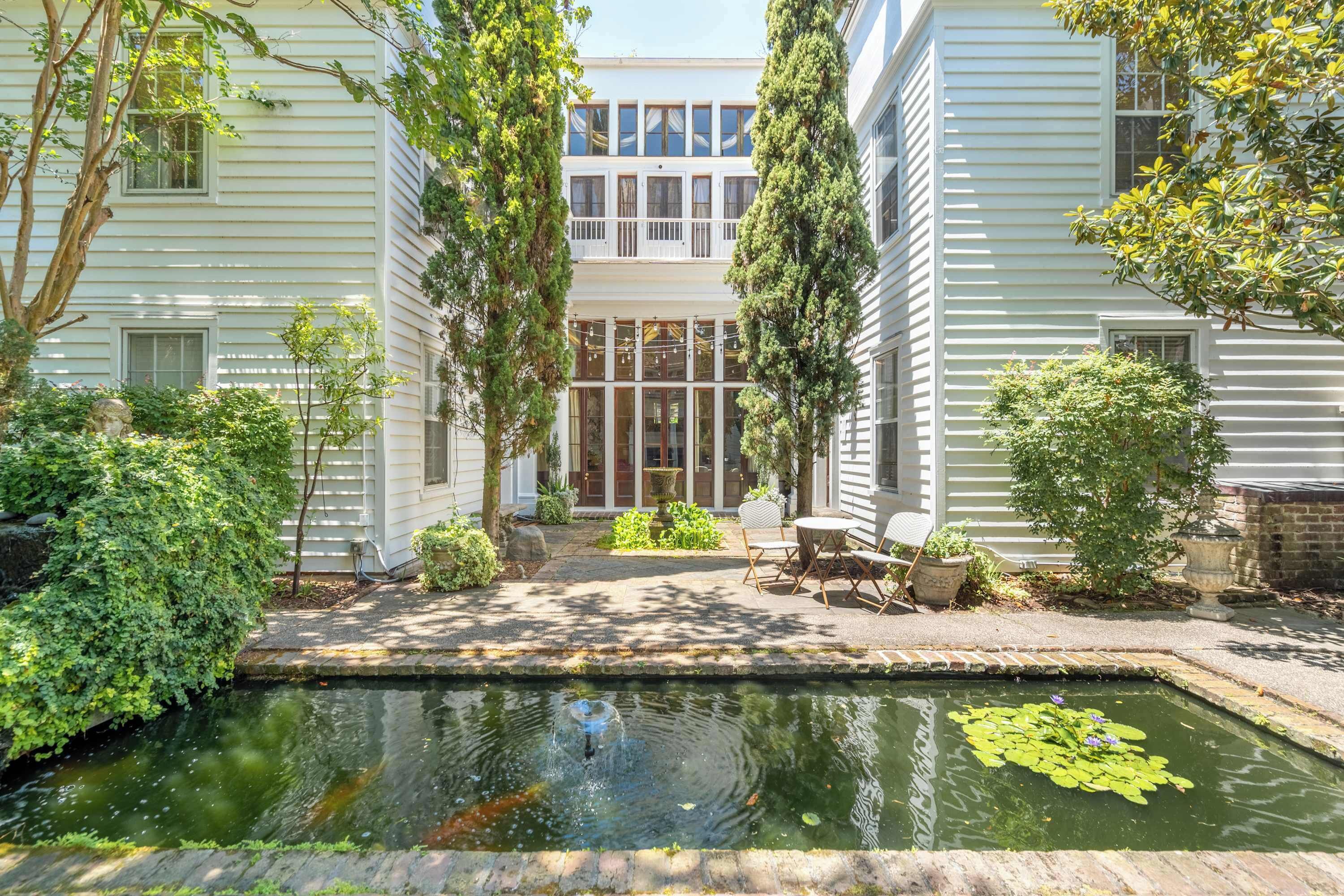 A two-story building with a courtyard featuring a small pond, outdoor seating, and a fountain.