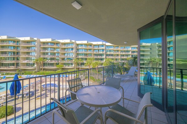 A balcony with a pool, lounge chairs, and a view of hotel buildings.