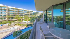 Uma varanda de hotel com piscina, palmeiras e vista para outros edifícios de hotéis.