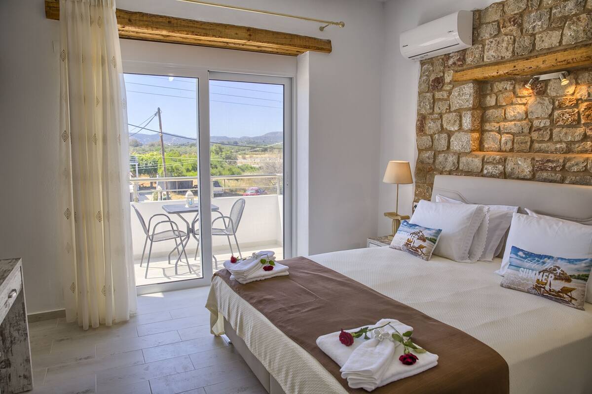 A hotel room with a bed, a balcony with chairs, and a stone wall.