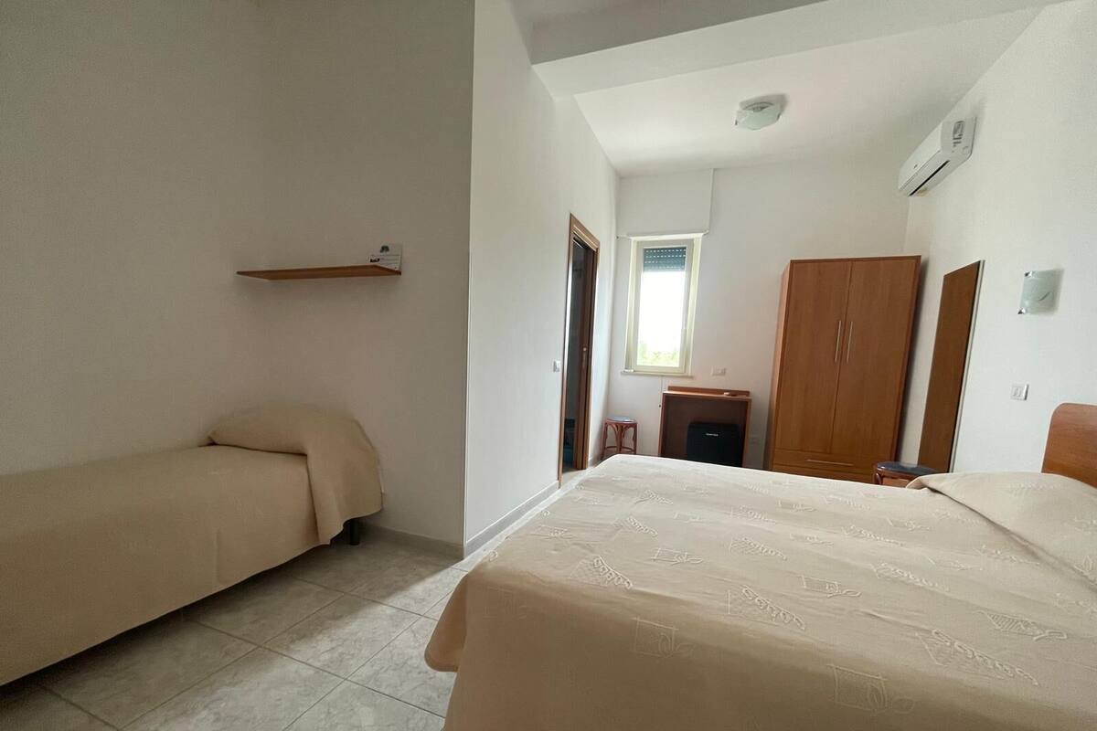 A bedroom with a bed, a smaller bed, a wardrobe, a desk, and a window.