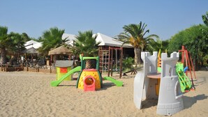 A beachside playground with a castle play structure, palm trees, and beach chairs.