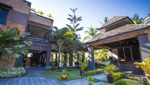Um edifício moderno com área externa coberta, plantas em vasos e calçada pavimentada.