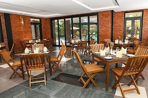 A restaurant with brick walls, large windows, and wooden tables and chairs. - Ocean Paradise Resort (Ngwe Saung)