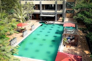 A rectangular pool with a surrounding deck, a building with multiple windows, and some greenery. - Ocean Paradise Resort (Ngwe Saung)
