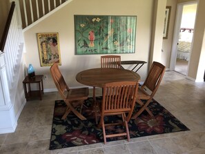 A dining area with a wooden table and chairs, a floral rug, and a painting of tropical birds on the wall. - Upscale Mauna Lani, 4BDRM, 2MSTR BTHS, 5 Beds for 8, Spacious W/Bikes Near Beach (Waimea)