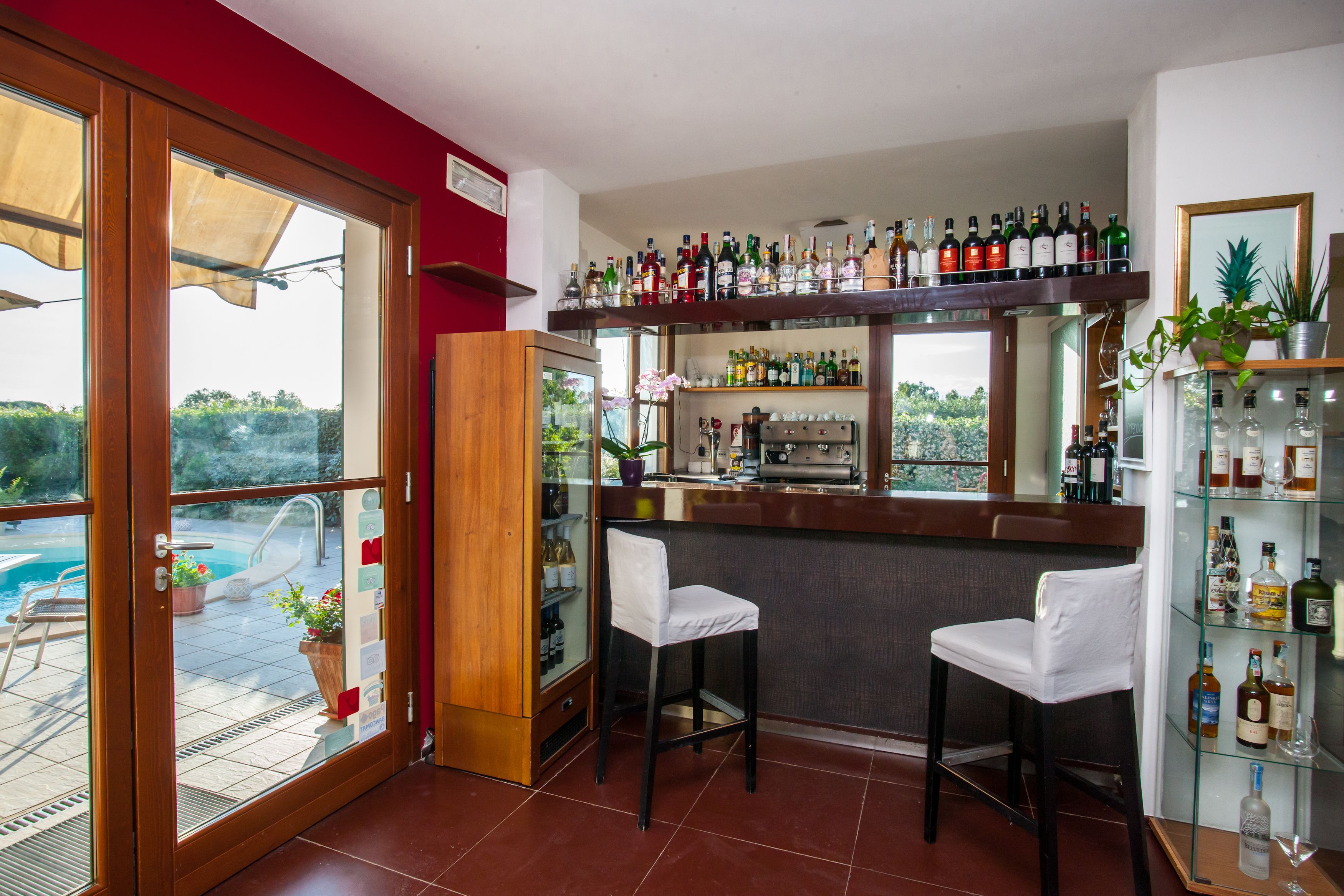 A bar area with a pool view, bar stools, and shelves of liquor bottles.