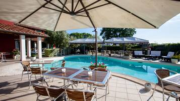 Un área de piscina con sillones, una mesa y sombrillas.