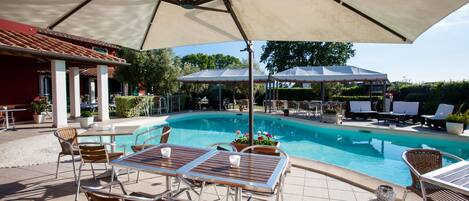 Un área de piscina con sillones, una mesa y sombrillas.