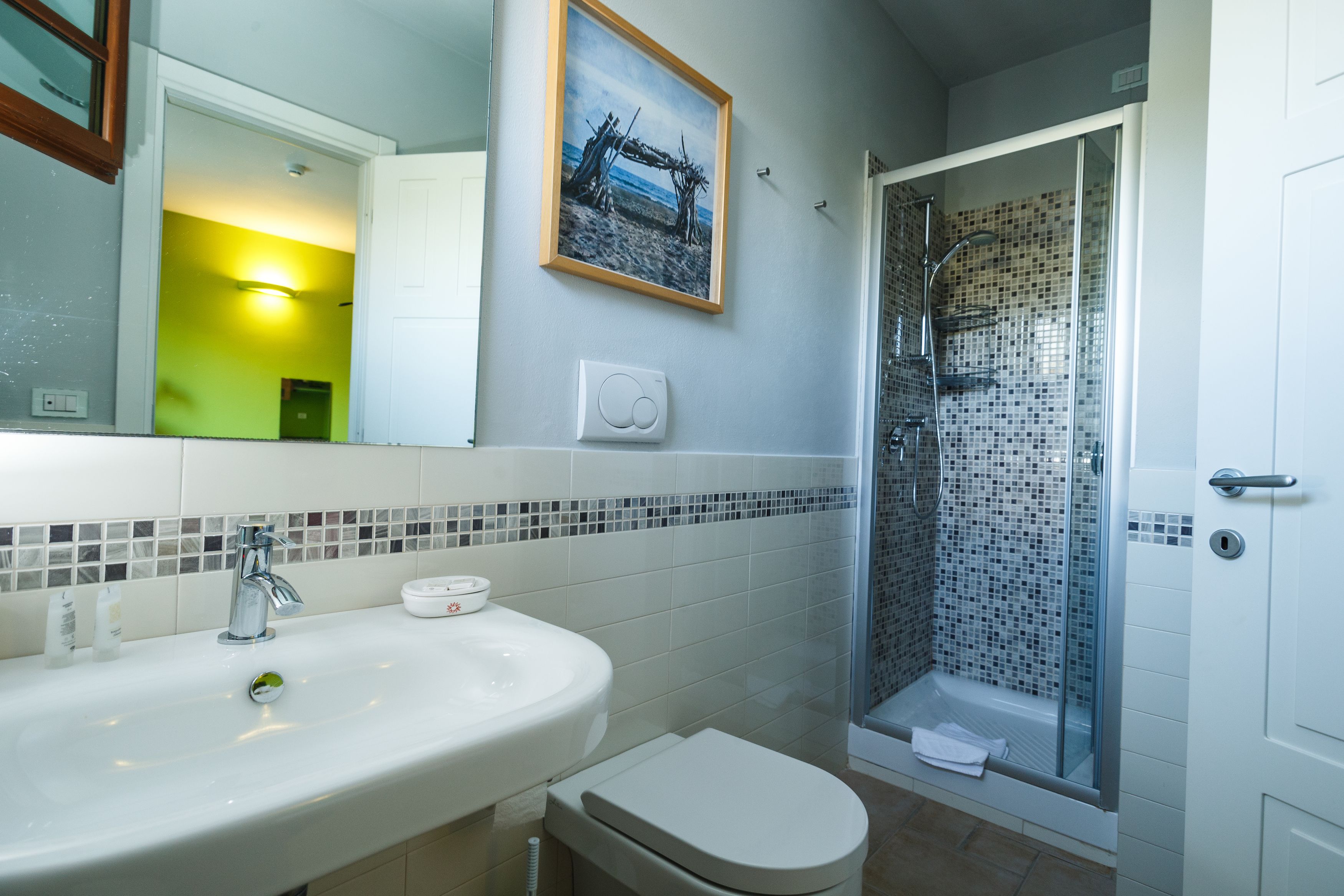 A bathroom with a sink, toilet, shower, and a framed picture on the wall.