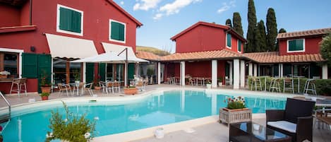 A swimming pool area with outdoor seating and red buildings.