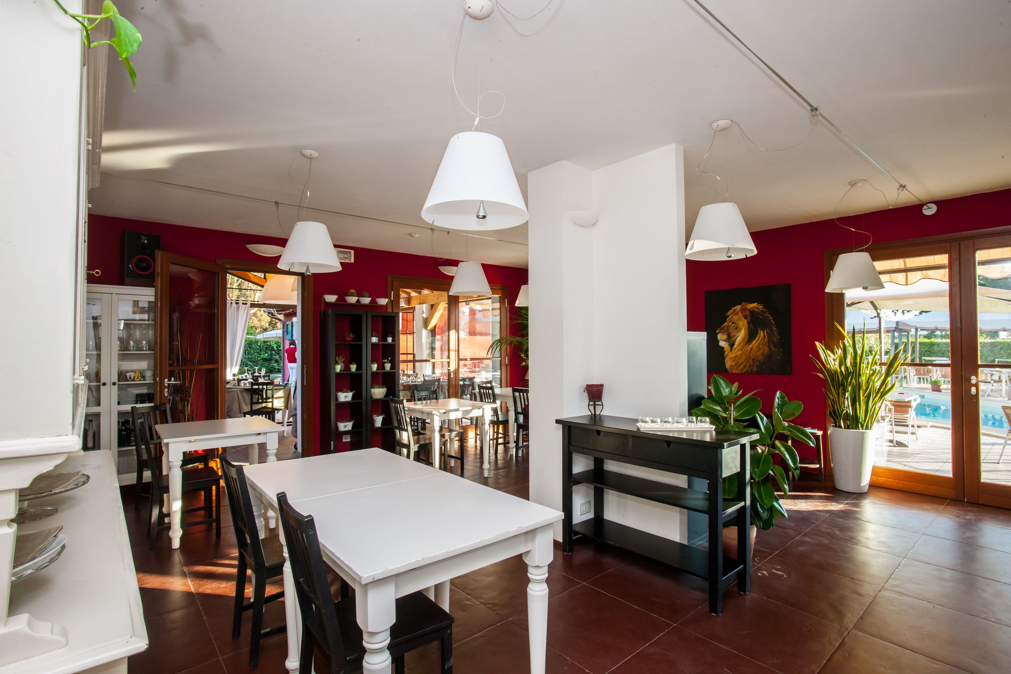 A dining area with white tables and chairs, a central black table with a vase, and a large potted plant.