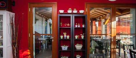 A restaurant interior with red walls, wooden shelves with potted plants, and a view of the outdoor seating area.
