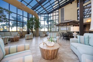 Relax in a spacious area with high ceilings and large windows, surrounded by comfortable seating and a modern design.