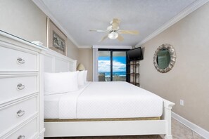 A bedroom with a bed, a dresser, a ceiling fan, a television, and a view of the outdoors.