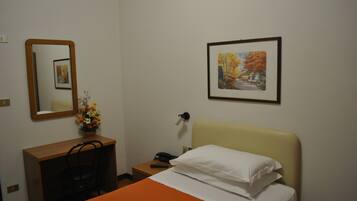 Quarto de hotel com uma cama, uma escrivaninha com cadeira, telefone, espelho e um quadro na parede.