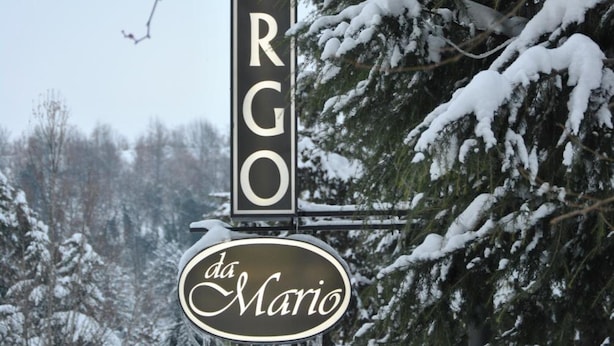 Un cartel con el nombre 'ALBERGO da Maria' en vertical, rodeado de árboles cubiertos de nieve.