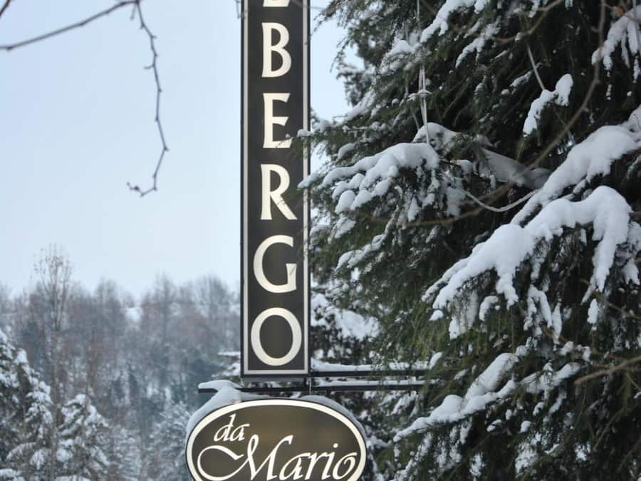 A sign with the name "ALBERGO da Maria" in a vertical format, surrounded by snow-covered trees.