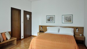 Una habitación de hotel con una cama, dos mesitas de noche, un banco de madera y dos cuadros en la pared.