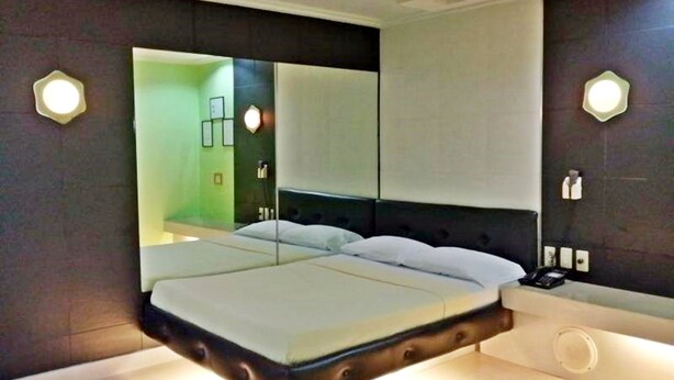 A modern bedroom with a large bed, a nightstand, and a wall-mounted mirror. - Orchids Drive Inn Hotel and Restaurant (Pasig)