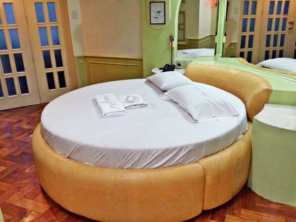 A circular bed with a beige upholstered headboard, a round bedside table, and a mirror on the wall. - Orchids Drive Inn Hotel and Restaurant (Pasig)