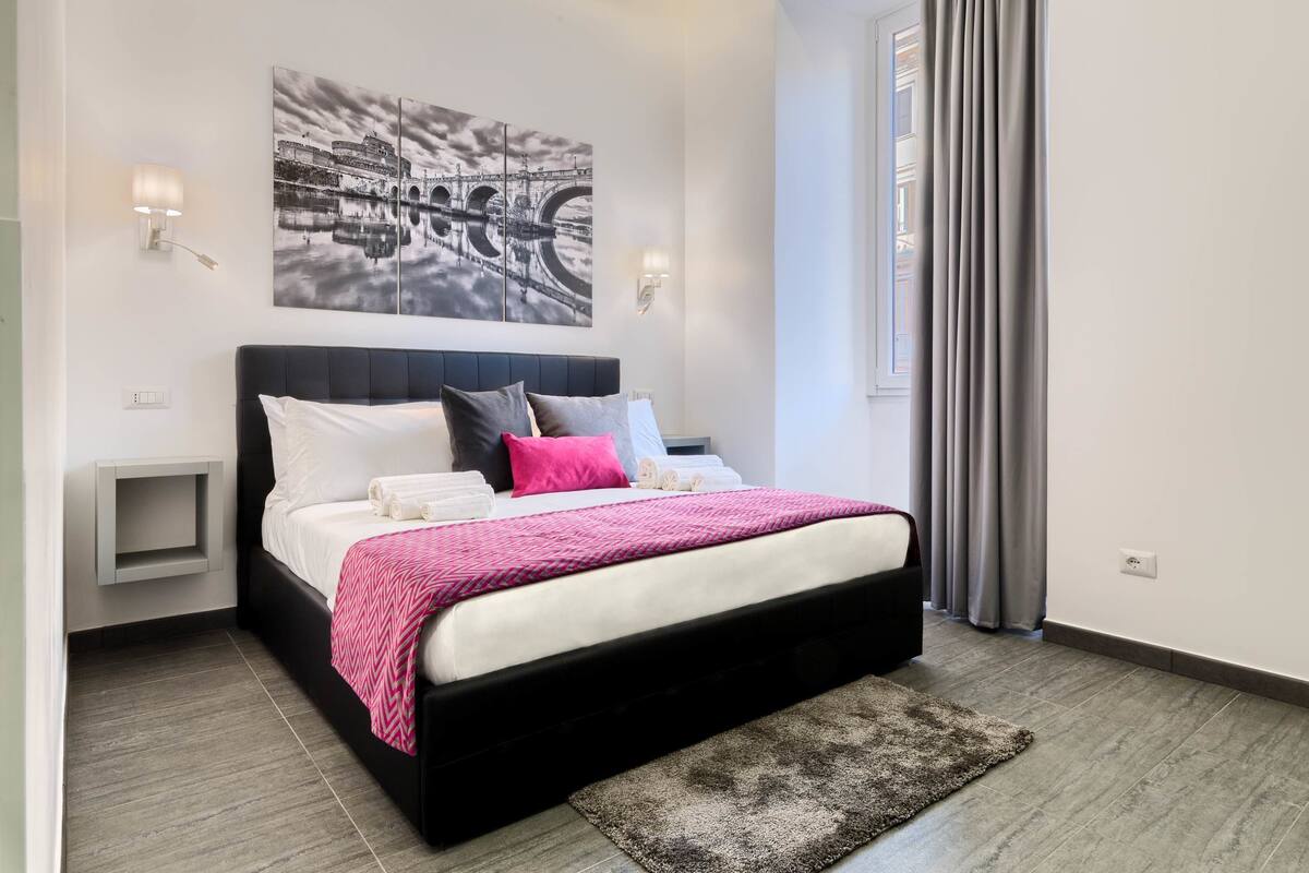 A modern bedroom with a large bed, a cityscape painting, and a view of the outdoors.