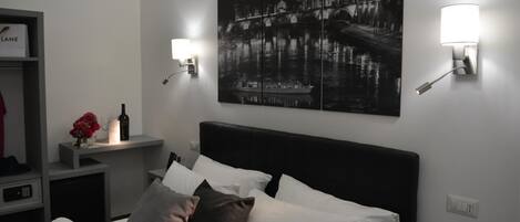 A hotel room with a bed, a nightstand, a wall-mounted lamp, and a framed picture of a cityscape.