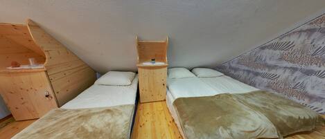 A compact room with two beds, a wooden wardrobe, and a small table.