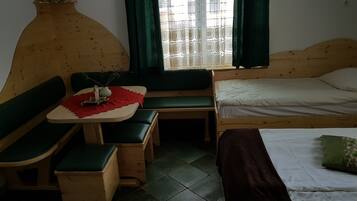 A cozy room with a wooden bed, a small table with a red cloth, a bench, and a window with green curtains.