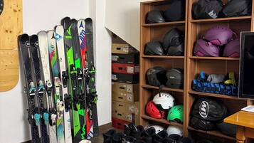 A room with skis, snowboards, and helmets on shelves and the floor.