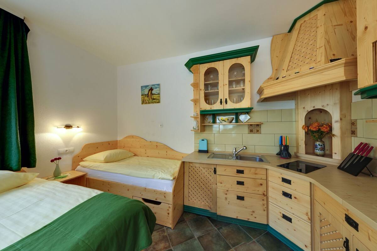 A compact room with a bed, a small kitchenette, and a window with curtains.
