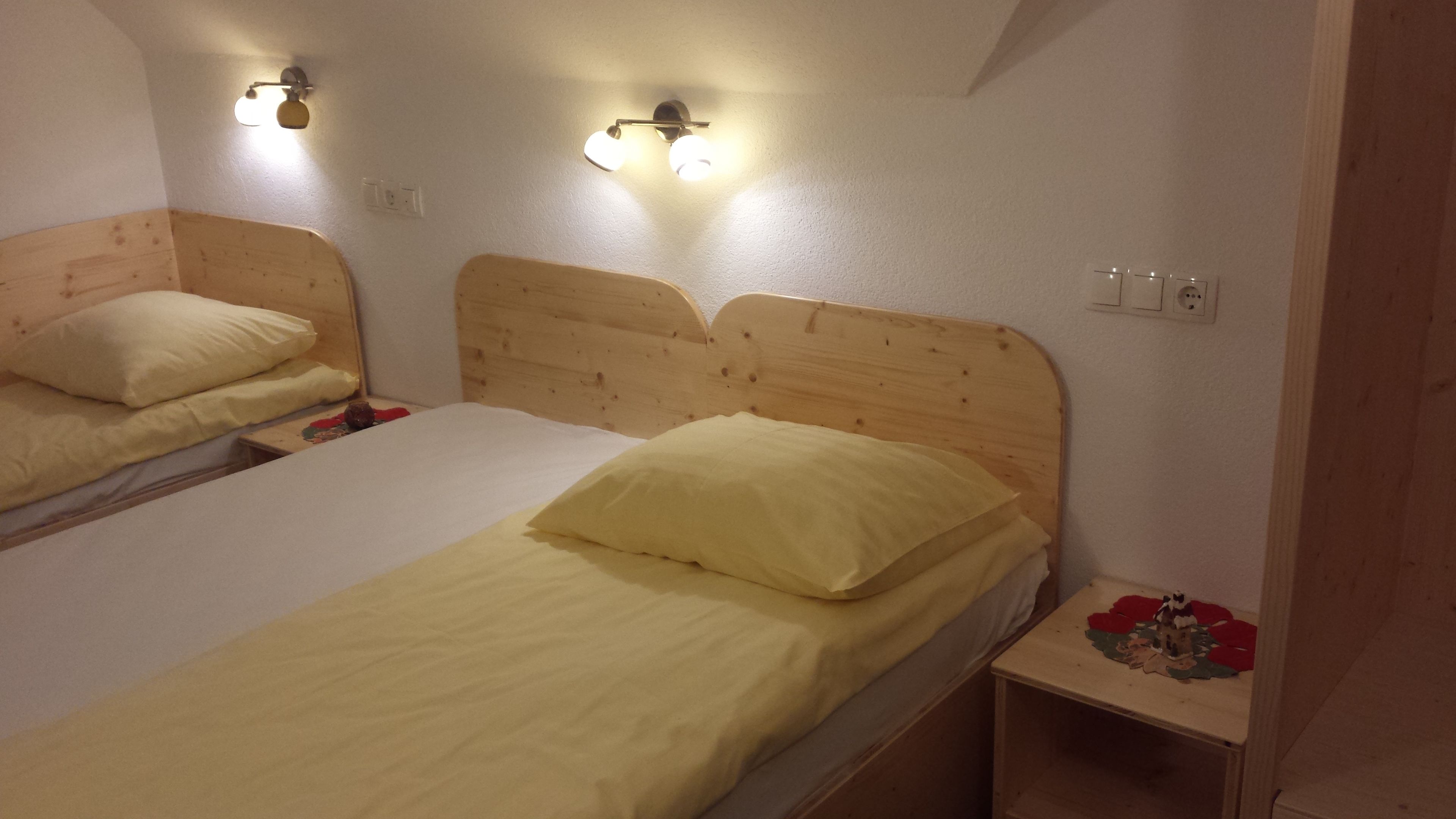 Ein Zimmer mit zwei Holzbettgestellen, jeweils mit Kopfstütze und Nachttisch. Darüber an der Wand befestigte Leuchten.