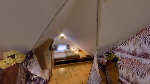 Un dormitorio cálido y acogedor en el ático, con techo inclinado, una cama individual, una mesita pequeña y una lámpara fijada a la pared.