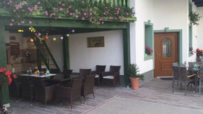 Eine Terrass mit Korbmöbeln, einer Holztreppe und einem grünen Geländer mit Blumen.