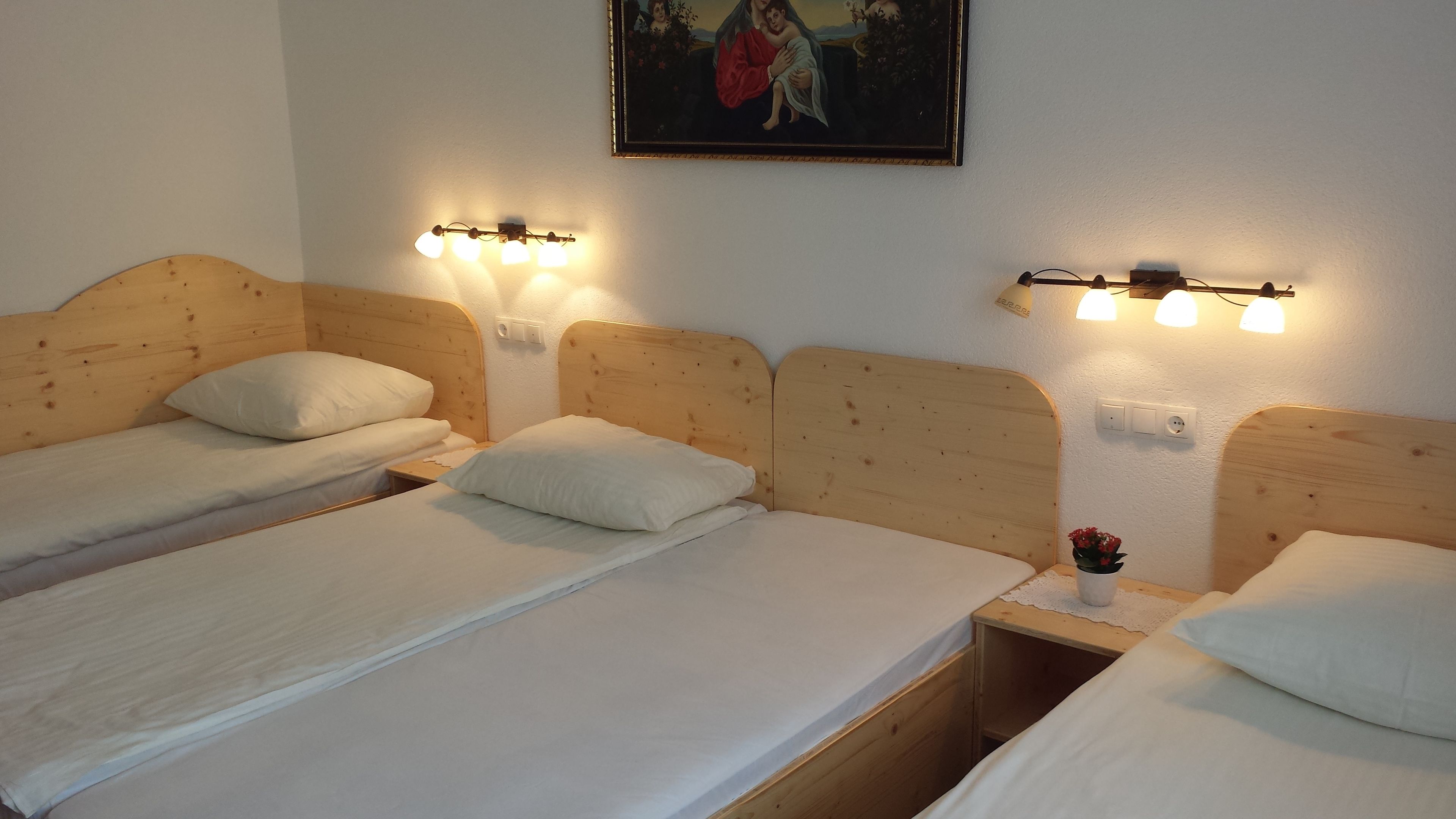 Une pièce comprenant trois lits en bois, chacun doté d’une tête de lit et d’une table de chevet. Des lampes murales sont fixées au-dessus de chaque lit.