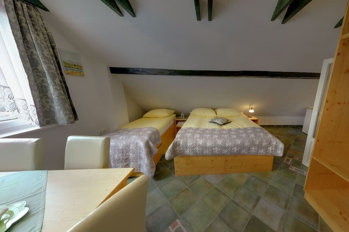 A small, cozy room with two beds, a wooden wardrobe, a desk, and a window with curtains.