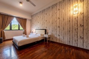 A neatly made bed with white linens, a bedside table with a lamp, and a wooden wall with a textured pattern. - Spacious Three Bedroom Condo Cyberjaya (Cyberjaya)