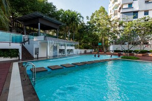 A swimming pool with a waterfall feature, surrounded by greenery and a covered area with stairs. - Spacious Three Bedroom Condo Cyberjaya (Cyberjaya)