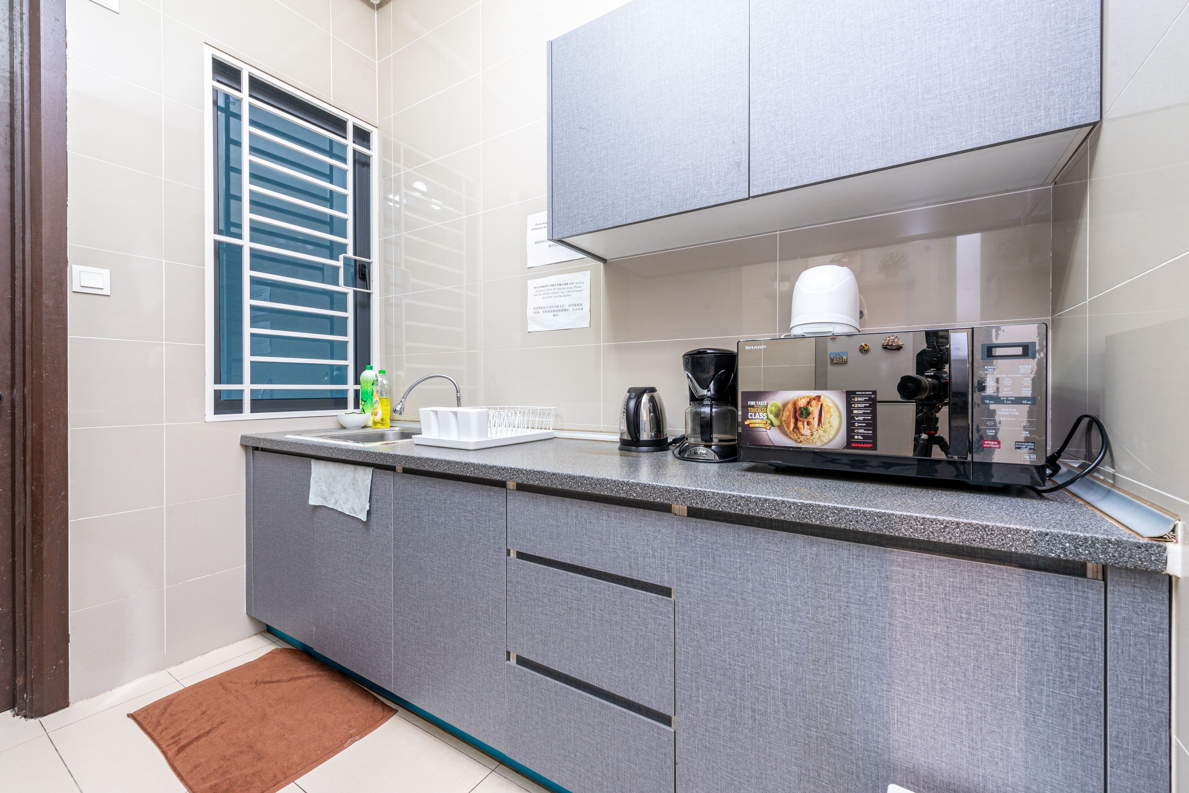 A modern kitchen with grey cabinets, a stainless steel coffee maker, and a window with blinds.