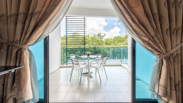 Un balcon avec une table et des chaises, une vue sur la verdure et un ciel dégagé.