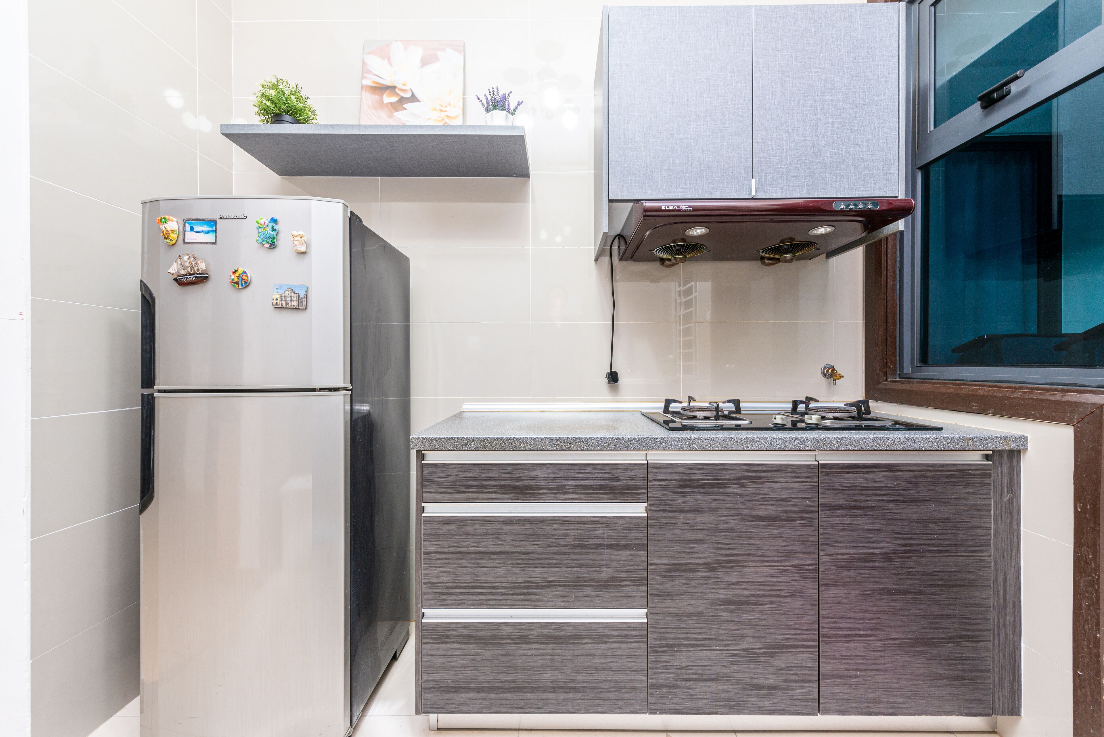 A kitchen with a stainless steel refrigerator, a built-in stove, and grey cabinetry.