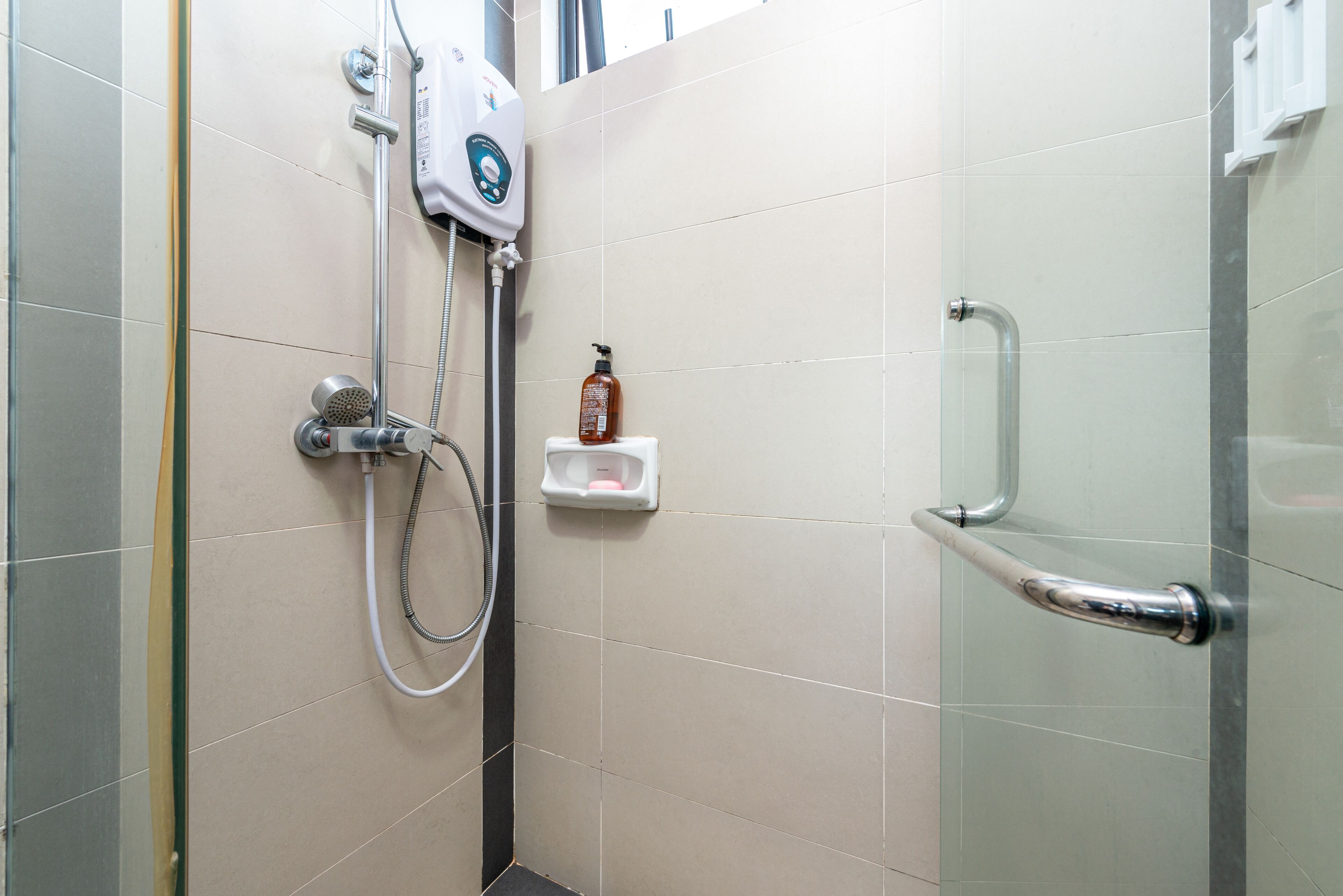 A bathroom with a shower, a soap dispenser, and a handrail.